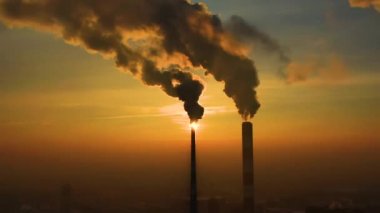 Hava kirliliği. Bitkinin bacalarından yükselen duman bulutları ve batan güneşin güzel sarı ışığı. İnsansız hava aracı çelik fabrikasının bacalarının üzerinde uçuyor..