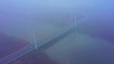 Hava aracı görüntüsü. Güneşli bir sabahta köprü. Sonbahar sisi havada, arabalar köprüden geçiyor..
