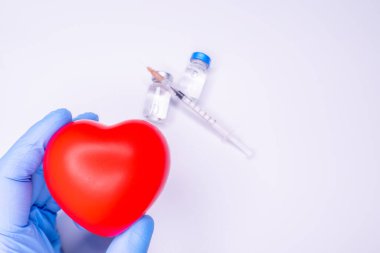 Tıbbi eldivendeki bir el, virüsün tüm dünyaya yayılmasını önlemek için icat edilen covid-19 aşısını içeren bir ampul taşıyor. Beyaz arka planda kırmızı kalpli bir maske