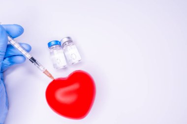 Tıbbi eldivendeki bir el, virüsün tüm dünyaya yayılmasını önlemek için icat edilen covid-19 aşısını içeren bir ampul taşıyor. Beyaz arka planda kırmızı kalpli bir maske