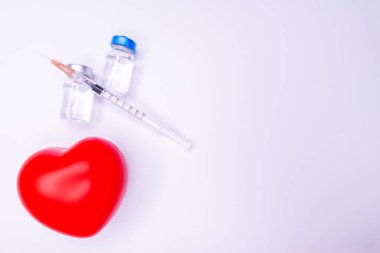 Tıbbi eldivendeki bir el, virüsün tüm dünyaya yayılmasını önlemek için icat edilen covid-19 aşısını içeren bir ampul taşıyor. Beyaz arka planda kırmızı kalpli bir maske