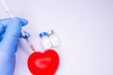 Tıbbi eldivendeki bir el, virüsün tüm dünyaya yayılmasını önlemek için icat edilen covid-19 aşısını içeren bir ampul taşıyor. Beyaz arka planda kırmızı kalpli bir maske