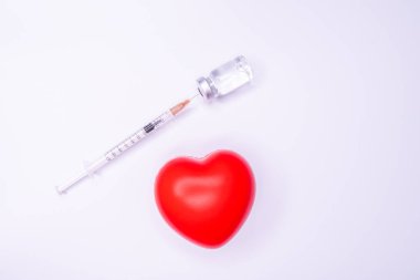 Tıbbi eldivendeki bir el, virüsün tüm dünyaya yayılmasını önlemek için icat edilen covid-19 aşısını içeren bir ampul taşıyor. Beyaz arka planda kırmızı kalpli bir maske