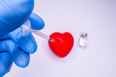 Tıbbi eldivendeki bir el, virüsün tüm dünyaya yayılmasını önlemek için icat edilen covid-19 aşısını içeren bir ampul taşıyor. Beyaz arka planda kırmızı kalpli bir maske