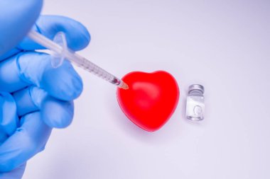 Tıbbi eldivendeki bir el, virüsün tüm dünyaya yayılmasını önlemek için icat edilen covid-19 aşısını içeren bir ampul taşıyor. Beyaz arka planda kırmızı kalpli bir maske