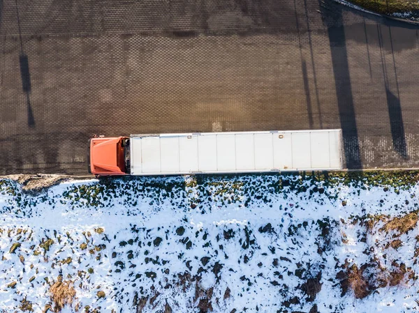 Aerial Follow Shot of White Semi Truck with Cargo Trailer Attached Moving Through Industrial Warehouse, Rural Area.