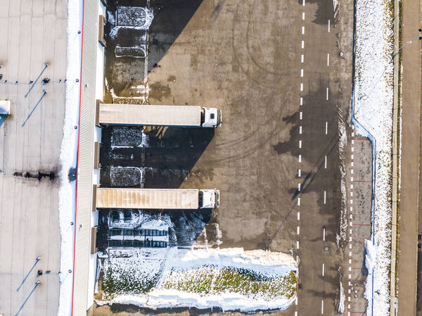 Aerial Follow Shot of White Semi Truck with Cargo Trailer Attached Moving Through Industrial Warehouse, Rural Area.