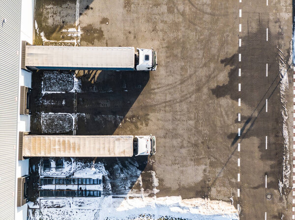 Aerial Follow Shot of White Semi Truck with Cargo Trailer Attached Moving Through Industrial Warehouse, Rural Area.