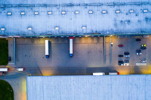 Aerial view of goods warehouse Night. Logistics center in industrial city zone from above. Aerial view of trucks loading at logistic center