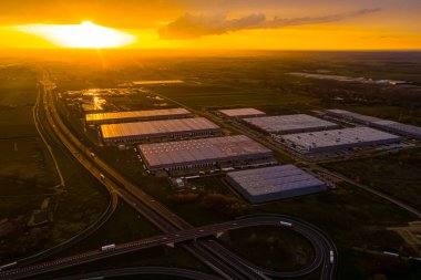 Depolu lojistik parkı, yükleme merkezi ve rampalarda yük ve boşaltma için bekleyen kargo karavanları olan bir sürü kamyonet gün batımında..