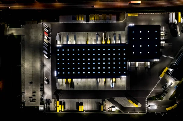 Night Aerial view of goods warehouse. Logistics center in industrial city zone from above. Aerial view of trucks loading at logistic center. View from drone.
