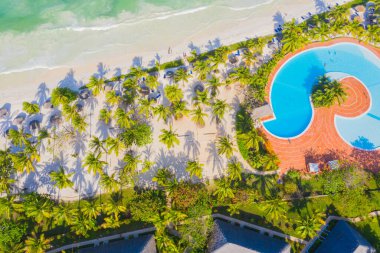 Güneşli bir günde tropikal kumsal manzarası, palmiyeler ve şemsiyelerle. Hint Okyanusu 'nda yaz tatili, Zanzibar, Afrika. Palmiye ağaçları, oteller, havuz, beyaz kum, gök mavisi deniz manzarası. Üst görünüm