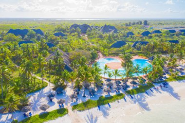 Güneşli bir günde tropikal kumsal manzarası, palmiyeler ve şemsiyelerle. Hint Okyanusu 'nda yaz tatili, Zanzibar, Afrika. Palmiye ağaçları, oteller, havuz, beyaz kum, gök mavisi deniz manzarası. Üst görünüm