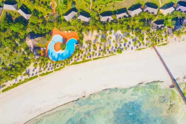 Aerial view of beautiful hotel in Indian ocean at sunset in summer. Zanzibar, Africa. Top view. Landscape with wooden hotel on the sea, azure water, sandy beach, green trees, boat. Luxury resort