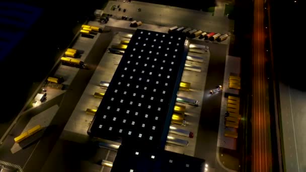 Aérien d'un parc logistique avec un hub de chargement. Les camions semi-remorques se tiennent aux rampes d'entrepôt pour le chargement et le déchargement de marchandises la nuit. — Video