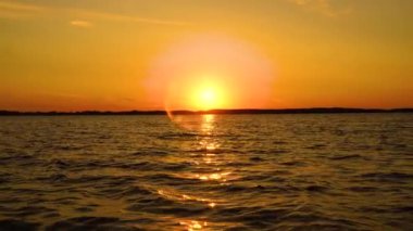 Gün batımında göl manzarası, gökyüzünde parlama ve sudaki gölün yanındaki ağaçların yansıması.,