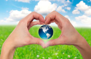 Hands holding green globe with grassy background - Stock Image clipart