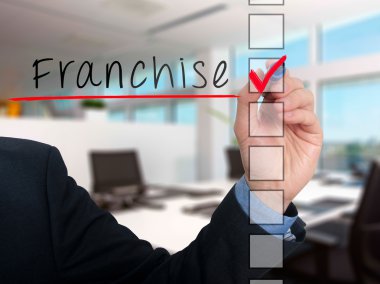 Businessman hand writing Franchise and check listing task. Isolated on blue background. Stock photo