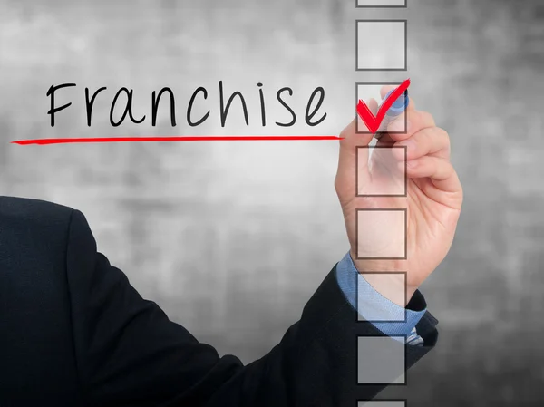 Businessman hand writing Franchise and check listing task. Isolated on blue background. Stock photo — Stock Photo, Image