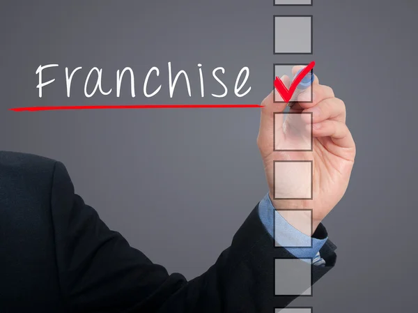 Businessman hand writing Franchise and check listing task. Isolated on blue background. Stock photo — Stok fotoğraf