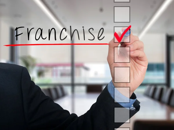 Businessman hand writing Franchise and check listing task. Isolated on blue background. Stock photo — Stock fotografie