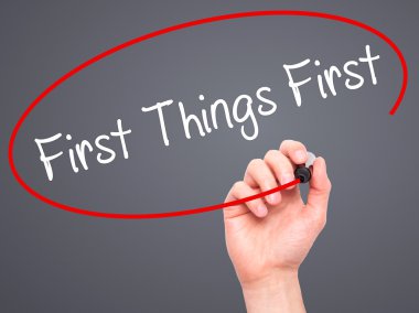 Man Hand writing First Things First with black marker on visual  clipart