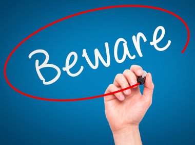 Man Hand writing Beware  with marker on transparent wipe board