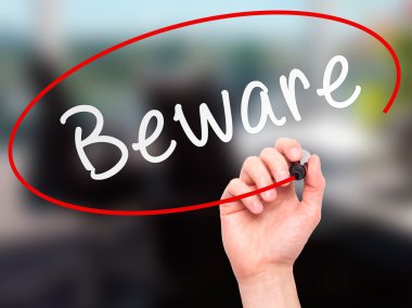 Man Hand writing Beware  with marker on transparent wipe board