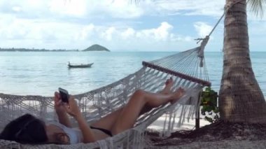 Sahilde bir hamakta cep telefonu kullanan rahat kadın