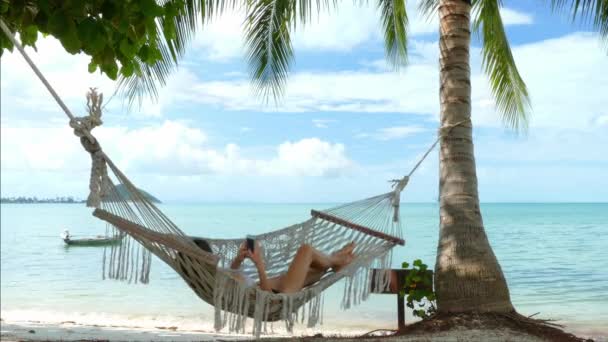 Frau benutzt Handy in einer Hängematte am Strand — Stockvideo