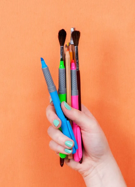 Frau Hand hält bunte Kunstwerkzeuge auf orangefarbenem Hintergrund — Stockfoto