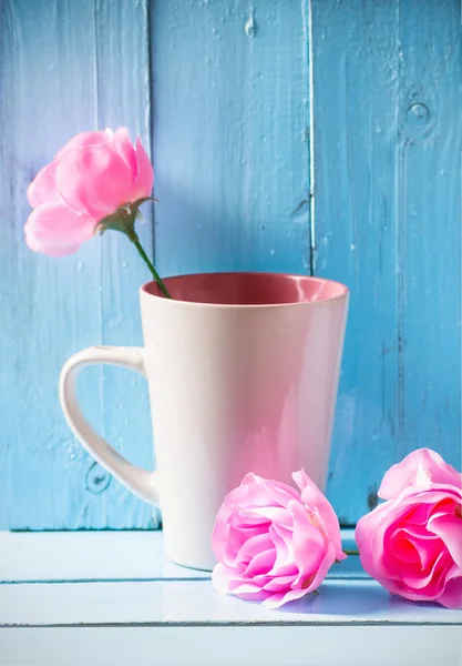 Mug with pink roses on blue wood background, still life — Stock Photo, Image