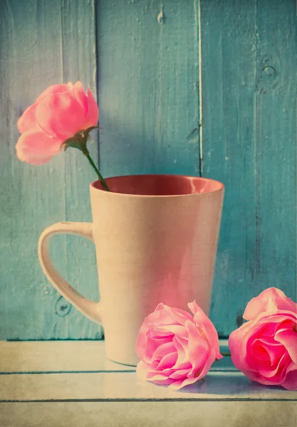 Vintage νεκρή φύση, κούπα με ροζ τριαντάφυλλα σε μπλε φόντο ξύλου — Φωτογραφία Αρχείου