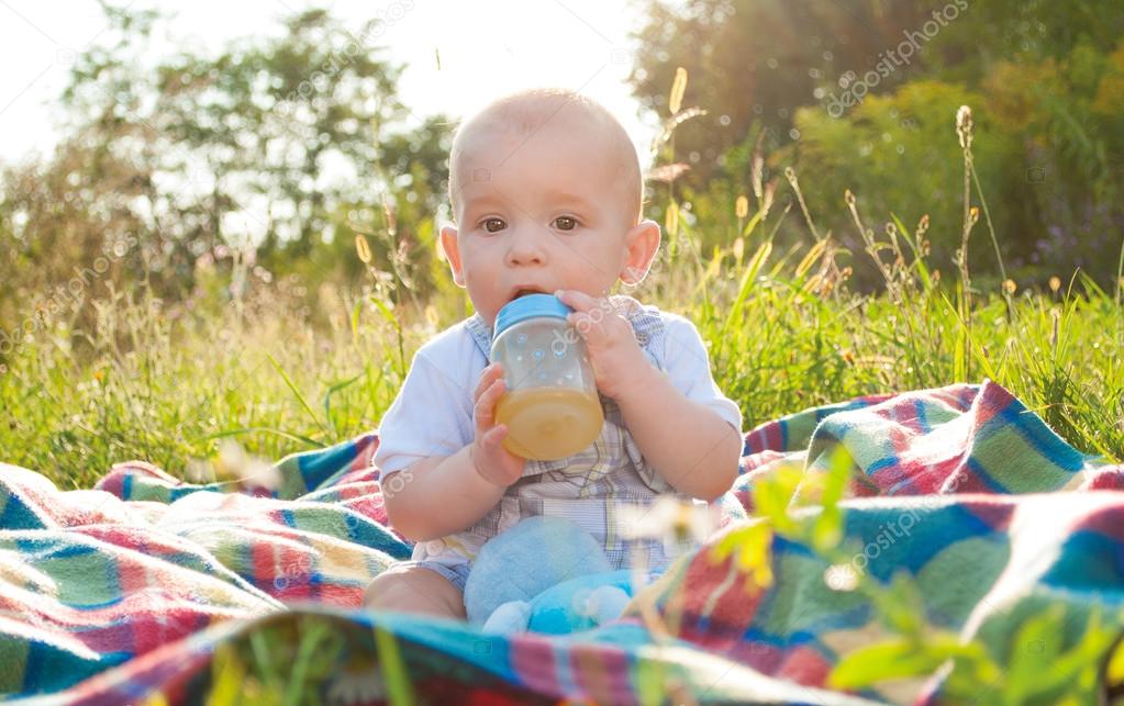 months old baby sitting on plaid and drinking juice — Stock