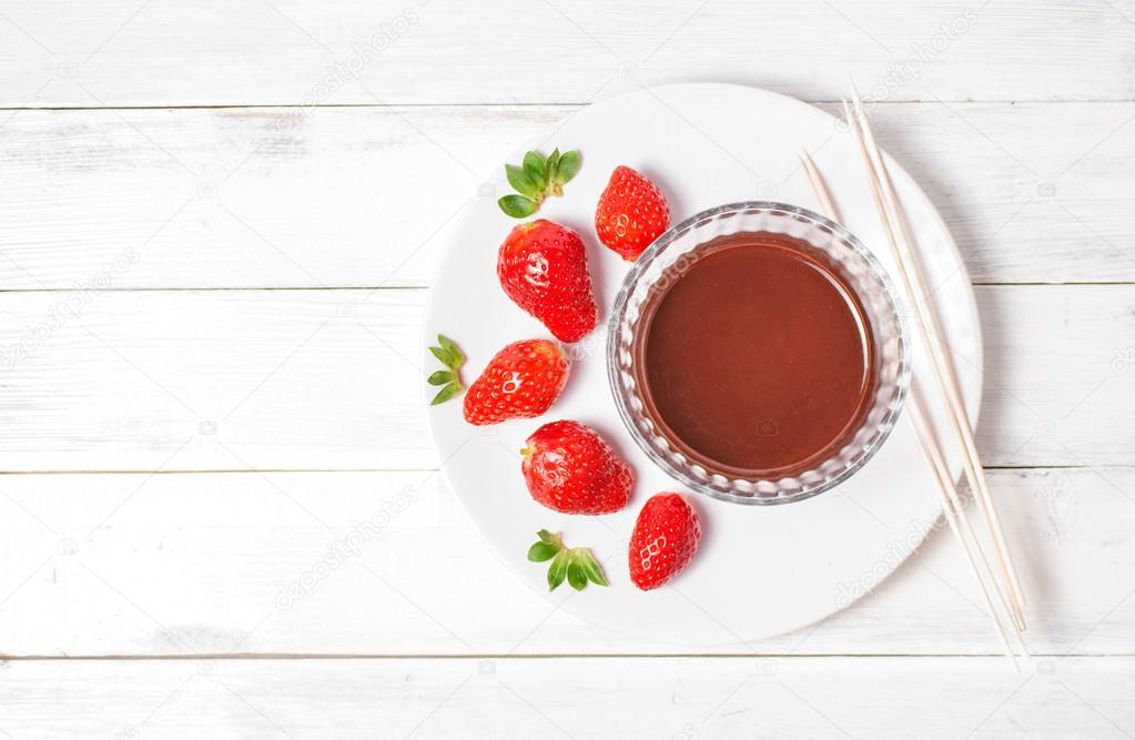 Strawberries and chocolate cream on white wood background, top view
