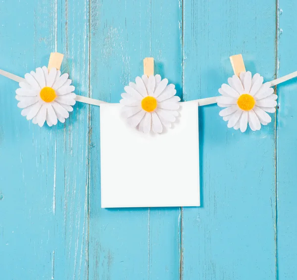 Chamomile flower clothespins with blank paper on blue wood background