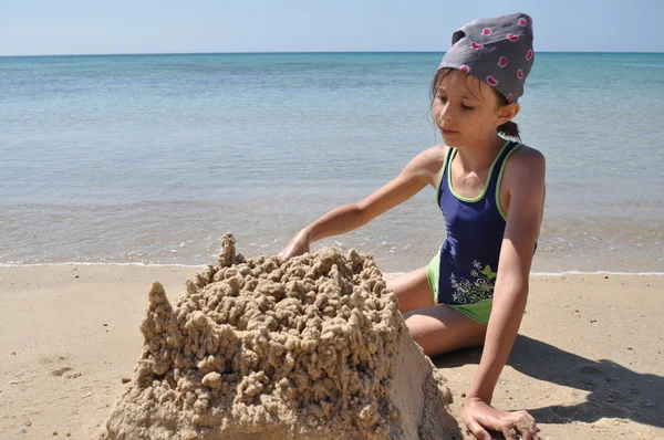 La ragazza costruisce un castello di sabbia sulla spiaggia. Vacanze in un paese esotico — Foto Stock