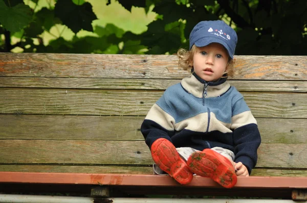 Junge in roten Gummistiefeln auf einer Schaukelbank sitzend. Verschlungene Reben schwingen. — Stockfoto
