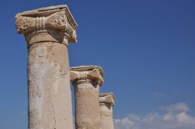 Yıpranmış dört taş sütun parlak mavi bir gökyüzüne karşı ayakta duruyor. Gündüz vakti tarihi bir yerde antik mimarinin işçiliğini vurguluyorlar..