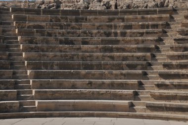 Amfitiyatroda, kırsal dokusunu ve tarihsel önemini gözler önüne seren yüksek bir sahne alanına çıkan aşınmış taş basamaklar yer alıyor. Güneş ışığı bu antik yapının detaylarını güçlendirir..