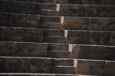 Güneş ışığı, eski bir amfitiyatronun yıpranmış taş basamaklarına gölge düşürür. Sahne, geçmişin ince ayrıntılarını ve dokusunu yakalıyor..