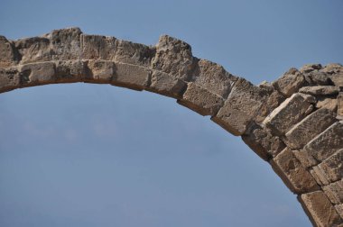 Büyük bloklardan oluşan etkileyici bir taş kemer yolu açık mavi bir gökyüzünde görülür. Bu yapı, antik mimari ve tarihi temsil ediyor..