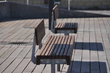 Kentsel bir bölgedeki ahşap bir güverteye iki basit kahverengi ahşap bank yerleştirilir. Banklar, güneş ışığı ve temiz bir çevre ile çevrili ahşap ve metalden yapılmıştır..
