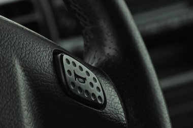 Yakından bakıldığında, yeni bir arabada dokulu yüzeyi olan bir direksiyon düğmesi vurgulanıyor. Arabanın iç kısmından yansıyan yumuşak ışık, parlak tasarımı ve modern özellikleri vurguluyor..