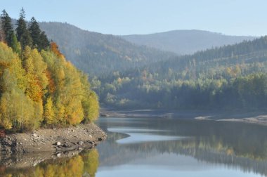 Sakin bir göl, berrak bir gökyüzünün altındaki sonbahar ağaçlarının canlı renklerini yansıtır. Çevredeki dağlar barışçıl bir zemin oluşturuyor. Açık hava aktiviteleri ve rahatlama için mükemmel..