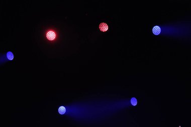Parlak kırmızı, mavi ve mor sahne ışıkları karanlık bir ortamda parlıyor ve gece gerçekleşen canlı bir olay için enerjik bir atmosfer yaratıyor..