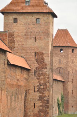 Ortaçağ şatosunun tuğlaları gri gökyüzüne çarpıyor. Yapıda belirgin kırmızımsı renkleri ve tarihi aurası olan klasik mimari sergileniyor..