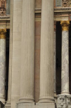 Zarif gri ve beyaz mermer sütunlar, klasik tasarım ve karmaşık altın detaylar sergileyen tarihi bir binada dimdik ayakta duruyor. Bu yapı canlı bir şehir bölgesinde yer almaktadır..