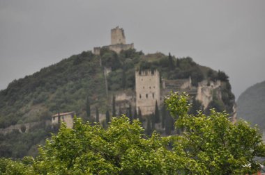 Manzarada ağaçlar ve yeşilliklerle kaplı bir tepede duran antik şato kalıntıları yer alıyor. Sahne atmosferik, kasvetli bir gökyüzünü yakalıyor ve tarihsel güzelliğe ekliyor..