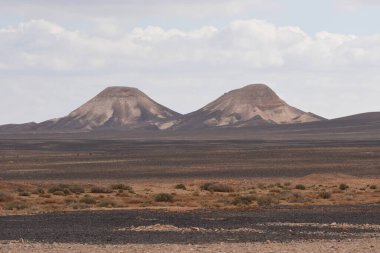 İkiz dağlar, düz çöl manzarasına hükmediyor. Pürüzsüz yamaçlarını bulutlara karşı sergiliyorlar. Arazi kuru ve kayalık, izolasyonun doğal güzelliğini vurguluyor..